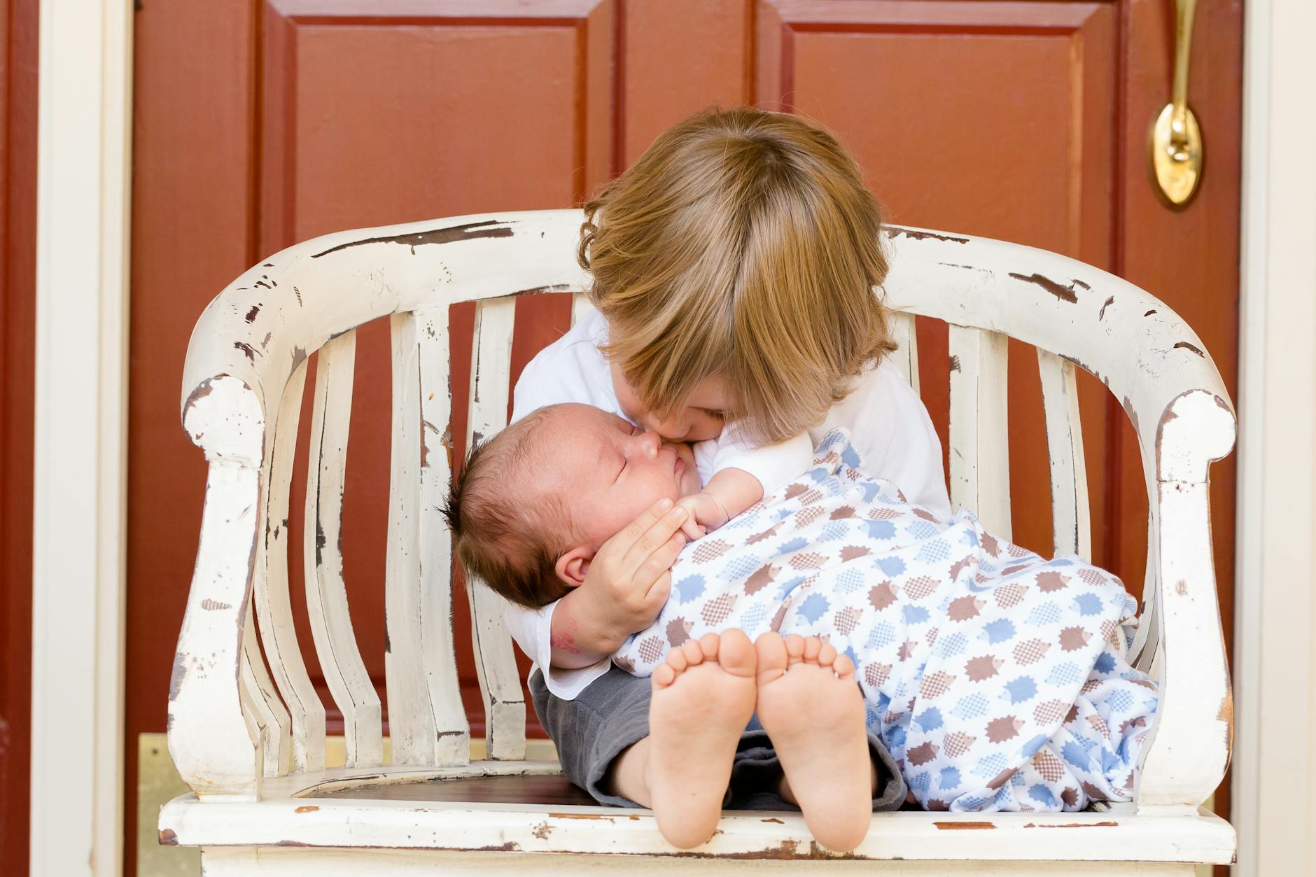 boy carrying and kissing baby sitting on chair